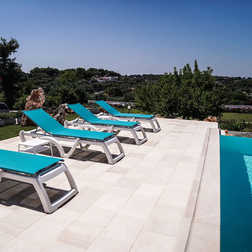 Arredamento esterno in stile mediterraneo per lamia e trullo in Puglia. Divani da giardino in vimini, ombrelloni colorati e tavolini in pietra per creare un'atmosfera accogliente